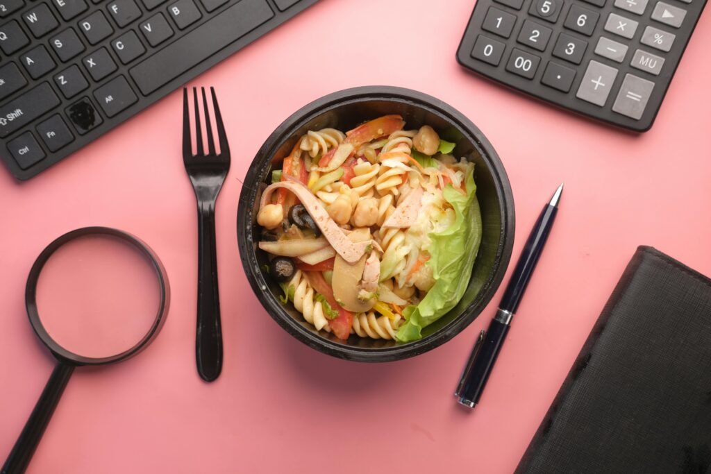 A vibrant pasta salad placed on a desk with office items, promoting healthy eating at work.